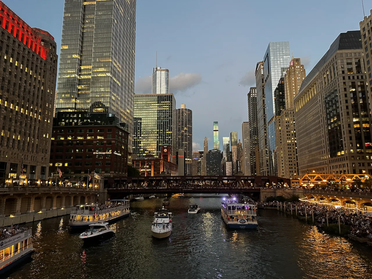 The Chicago River at dusk, downtown towers lit with golden light on both banks, boats in the river